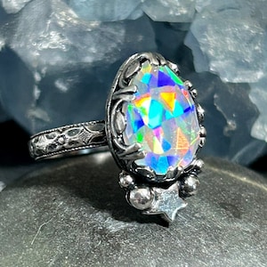 May include: A silver ring with a large iridescent oval gemstone set in a detailed silver setting. The ring band is decorated with a floral pattern.