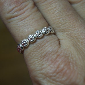 May include: A silver ring with a row of small, textured, round beads.