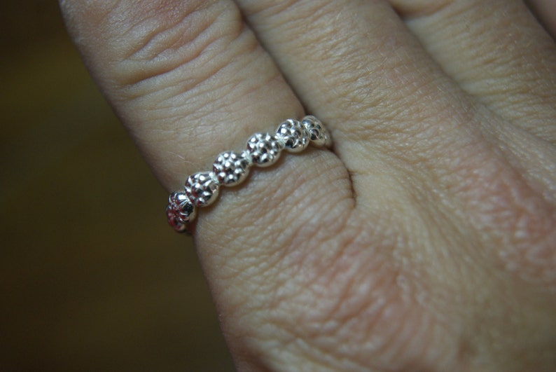 May include: A silver ring with a row of small, textured, round beads.
