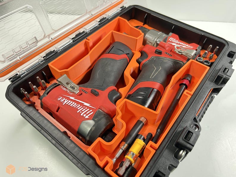 May include: A black and orange tool case containing two red and black power drills and various drill bits. The drills are labelled "Milwaukee". The case has a clear lid and orange interior compartments.