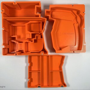 Puede incluir: Tres moldes de pl&aacute;stico naranja para hacer una herramienta. Los moldes est&aacute;n vac&iacute;os y tienen varios compartimentos. El molde de la derecha tiene el texto "FCS Designs".