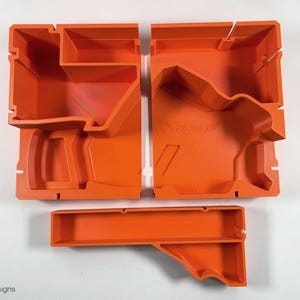 May include: Orange plastic storage organizer with multiple compartments. The organizer is divided into three sections, each with a different shape. The organizer is designed to hold small items, such as tools, craft supplies, or electronics.