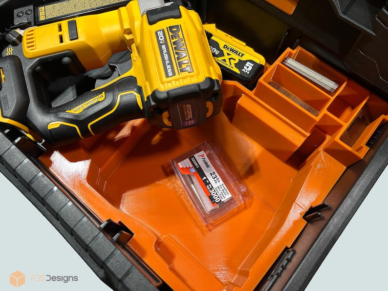 Peut inclure: Un cloueur sans fil DeWalt 20V jaune et noir et un bloc-batterie sont dans un organisateur d'outils orange et noir. Un paquet d'agrafes de calibre 23 de 2,54 cm est &eacute;galement visible.