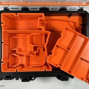 Puede incluir: Una caja de herramientas negra abierta con insertos de espuma naranja. Los insertos est&aacute;n dise&ntilde;ados para contener varias herramientas y accesorios.