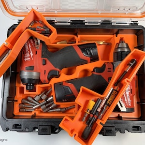 May include: Two orange and black tool organizers with two red and black cordless drills and a variety of drill bits. The organizers are labeled "Milwaukee" and "DeWalt".