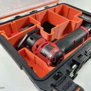 以下が含まれることがあります： 黒と赤の電動工具とバッテリー、キャリングケース。工具はケースのカスタムフォームインサートに入っています。ケースは黒でオレンジのアクセントが付いています。