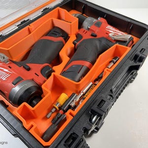 May include: A black and orange tool case with two red and black cordless drills and various bits inside. The drills are labeled "Milwaukee".