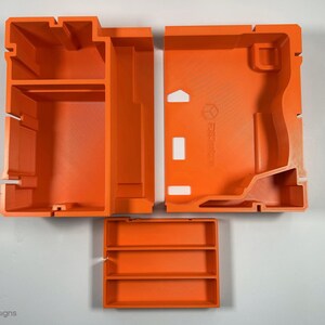 May include: Three orange plastic storage containers with compartments. The containers are designed to fit together to create a larger storage unit.