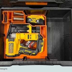 Peut inclure: Une bo&icirc;te &agrave; outils noire et orange avec un cloueur jaune et noir, une batterie et des compartiments de rangement. Le cloueur est un mod&egrave;le sans fil avec une poign&eacute;e noire et un corps jaune. La batterie est &eacute;tiquet&eacute;e "20V" et "5 Ah".