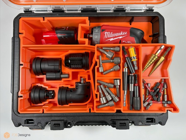 Puede incluir: Una caja de herramientas naranja y negra con un taladro Milwaukee FUEL y varios brocas y accesorios. La caja tiene varios compartimentos para organizar las herramientas.