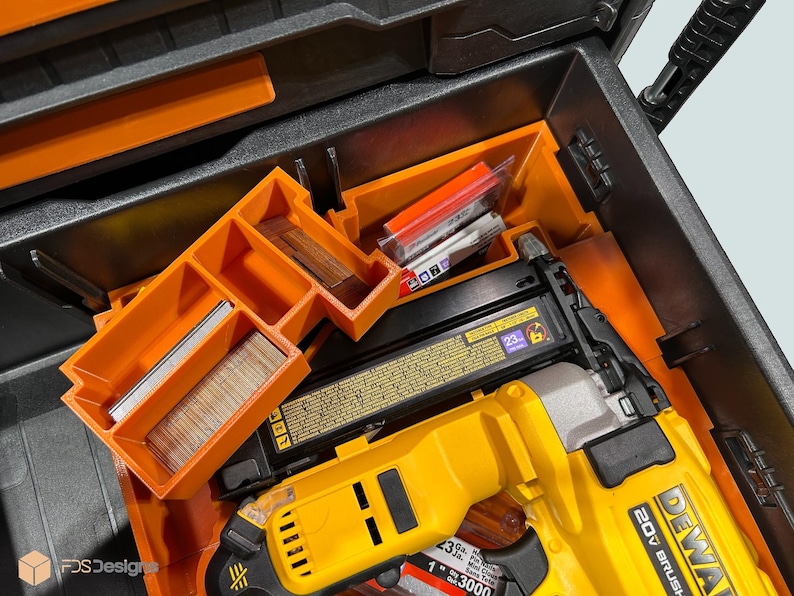 Peut inclure: Une bo&icirc;te &agrave; outils noire ouverte avec des compartiments orange et un cloueur Dewalt 20V Brushless jaune et noir. La bo&icirc;te contient divers clous et fixations, rang&eacute;s dans des plateaux orange.