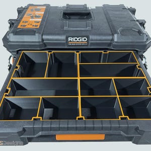 May include: A black and orange RIDGID Pro Gear System 2.0 tool storage box with a pull-out drawer. The drawer is divided into multiple compartments with yellow dividers. The box has a handle and the brand name is visible.