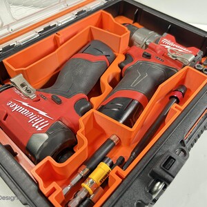 May include: An open black and orange tool case containing red and black power tools. The case holds two red and black Milwaukee FUEL drills, drill bits, and other tools. The tools are neatly arranged within the case.