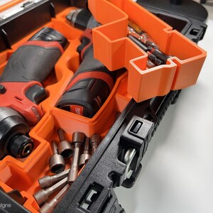 May include: Two red and black cordless power drills with a black and orange carrying case. The drills are in the case with a variety of drill bits.