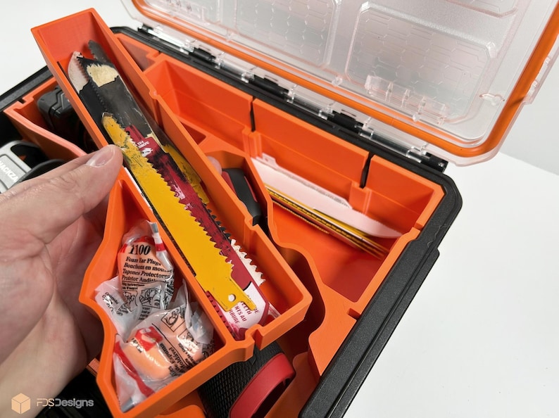 May include: An orange and black toolbox with a clear lid open. The toolbox is filled with various tools, including a saw blade, earplugs, and a small knife. The toolbox is made of durable plastic and has a sturdy handle.