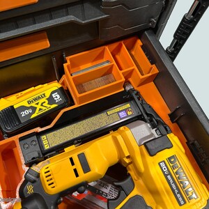Peut inclure: Un cloueur sans balai DeWalt 20V jaune et noir et une batterie sont rang&eacute;s dans un organiseur d'outils orange et noir. L'organisateur comporte plusieurs compartiments pour les outils et accessoires. La batterie est &eacute;tiquet&eacute;e 5 AH.