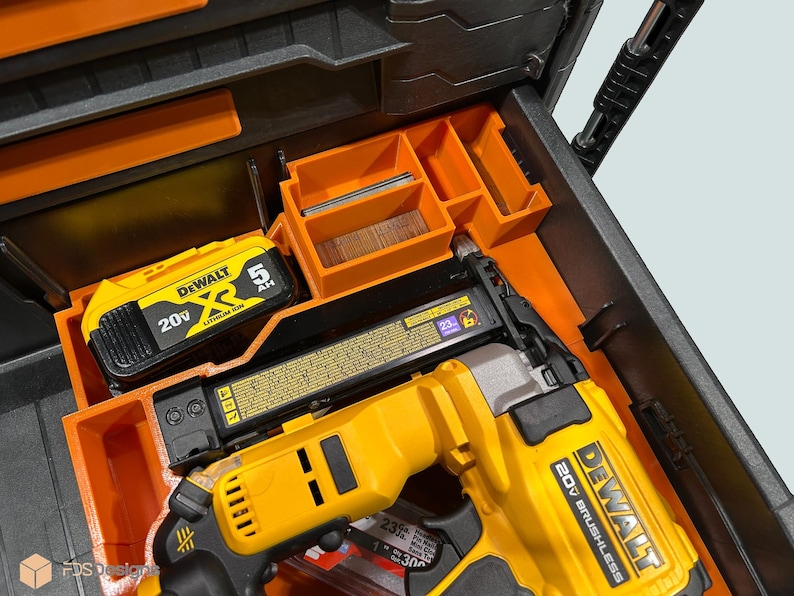 Peut inclure: Un cloueur sans balai DeWalt 20V jaune et noir et une batterie sont rang&eacute;s dans un organiseur d'outils orange et noir. L'organisateur comporte plusieurs compartiments pour les outils et accessoires. La batterie est &eacute;tiquet&eacute;e 5 AH.