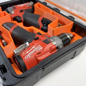 May include: Two red and black cordless drills with the Milwaukee logo are stored in a black and orange hard case with a clear lid.