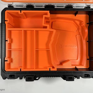 Puede incluir: Una caja de herramientas negra abierta con un inserto de espuma naranja. El inserto tiene varios compartimentos y un gran recorte para una herramienta. El texto "FORTRESS" est&aacute; impreso en la espuma.
