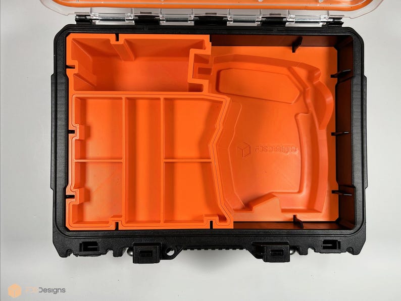 Puede incluir: Una caja de herramientas negra abierta con un inserto de espuma naranja. El inserto tiene varios compartimentos y un gran recorte para una herramienta. El texto "FORTRESS" est&aacute; impreso en la espuma.