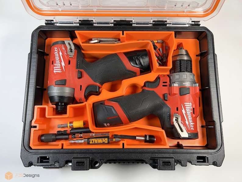 May include: Two Milwaukee power drills, one red and black impact driver and one red and black drill, are stored in a black and orange hard plastic case. The case has a compartment for storing additional drill bits and accessories. The case is open and the drills are visible.