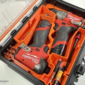 May include: A black and orange tool case with a clear lid, containing red and black power tools and various drill bits. The tools are labelled "Milwaukee" in white lettering. The case is organised with orange inserts.