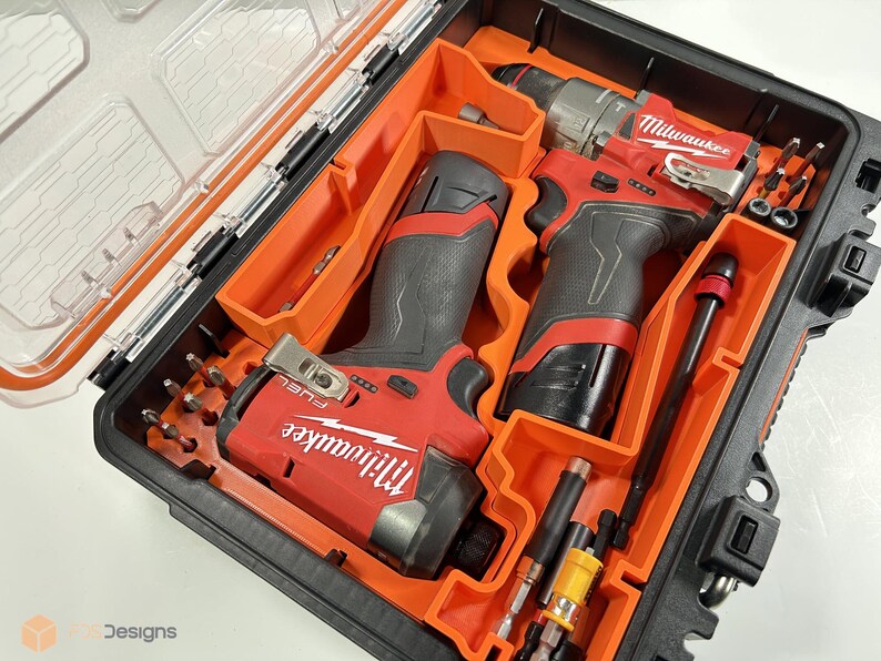 May include: A black and orange tool case with a clear lid, containing red and black power tools and various drill bits. The tools are labelled "Milwaukee" in white lettering. The case is organised with orange inserts.