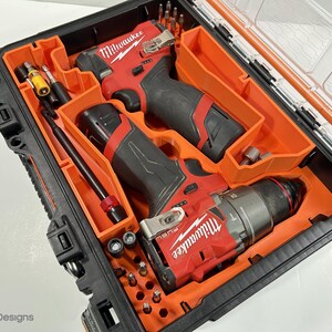 May include: Black and orange tool case containing two red and black power drills and various drill bits. The drills are labelled "Milwaukee" and "FUEL". The case has a clear lid and is designed for tool organisation.