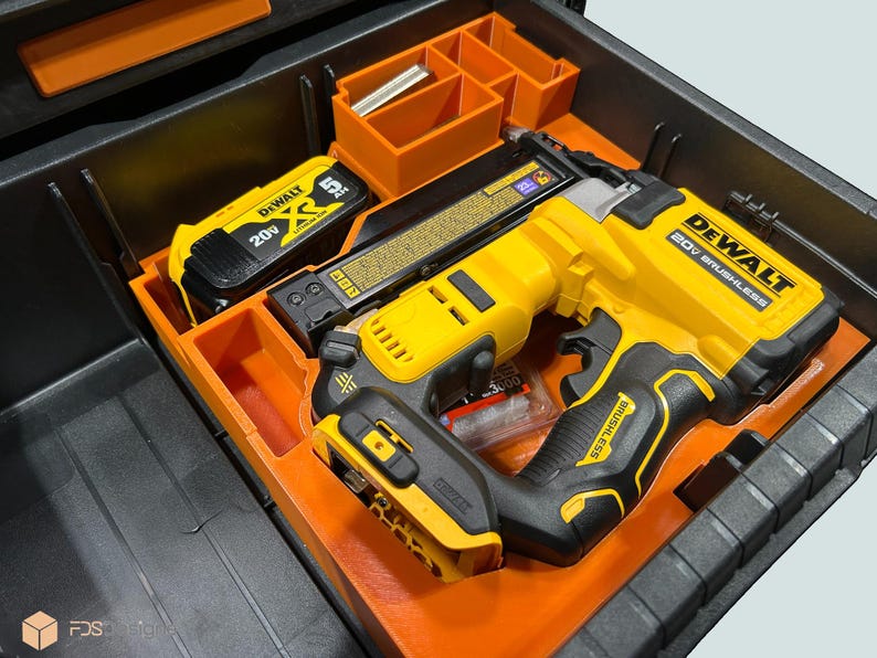 Peut inclure: Un cloueur sans fil DeWalt 20V sans balai jaune et noir et une batterie sont rang&eacute;s dans un organisateur orange &agrave; l'int&eacute;rieur d'une bo&icirc;te &agrave; outils noire. La bo&icirc;te &agrave; outils comporte des compartiments de rangement orange suppl&eacute;mentaires.