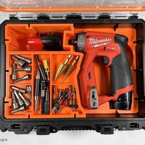 Puede incluir: Una caja de herramientas naranja y negra con un taladro Milwaukee FUEL rojo y negro y varios brocas y accesorios.