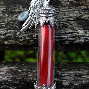 May include: A silver pendant featuring a red feather encased in a glass vial. The pendant is decorated with a silver angel wing and a silver crown.