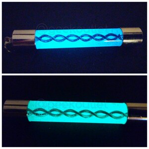 Puede incluir: Un llavero que brilla en la oscuridad con una tapa de metal plateado y un tubo transparente lleno de un l&iacute;quido azul que gira.