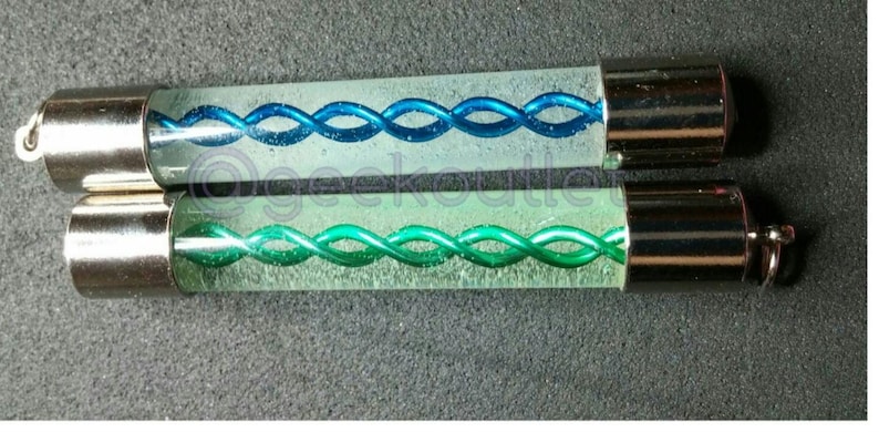 Puede incluir: Dos tubos de vidrio con tapas plateadas. Los tubos contienen un l&iacute;quido transparente con una espiral azul y verde en su interior.