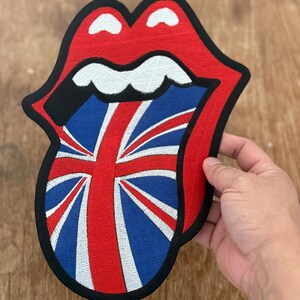 May include: An embroidered patch of a tongue sticking out with a Union Jack flag design, in red and black.