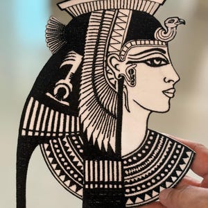 Könnte beinhalten: Schwarz-weiß gestickter Bügelaufkleber mit einer ägyptischen Königin, die eine Krone und eine Halskette trägt. Die Königin blickt nach rechts.