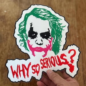 Könnte beinhalten: Weißer Stoff-Patch mit einem grünen und schwarzen Bild des Jokers aus dem Film "The Dark Knight" mit dem Text "WHY SO SERIOUS?" in Rot.