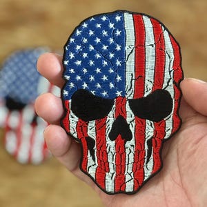 Op de afbeelding: Een geborduurde patch van een schedel met het ontwerp van de Amerikaanse vlag. De schedel is rood, wit en blauw met zwarte ogen.