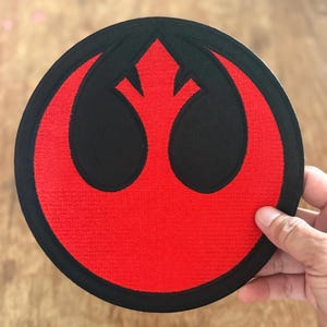 May include: A red and black embroidered patch featuring the Rebel Alliance symbol from Star Wars.