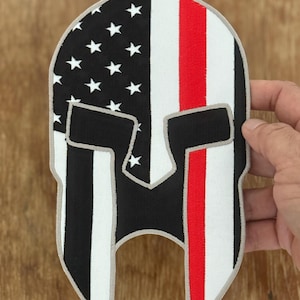 Op de afbeelding: Een geborduurde patch met een Spartaans helm-ontwerp met een Amerikaanse vlag en een dunne rode lijn.