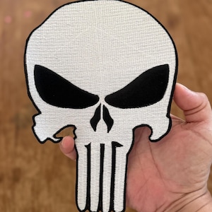 Peut inclure: Patch de crâne blanc avec des yeux noirs et un contour noir. Le crâne a un bord irrégulier et cinq lignes verticales sous le nez.
