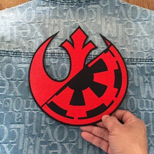May include: A red and black embroidered patch featuring the Rebel Alliance symbol and the Imperial symbol, split in half. The patch is sewn onto a blue denim jacket.