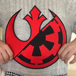 Op de afbeelding: Een geborduurde patch met het Rebel Alliance-symbool en het Imperial-symbool, doormidden gesplitst in rood en zwart.