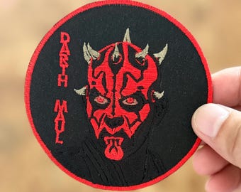 Può includere: Una toppa ricamata rossa e nera con il testo "Darth Maul" e un primo piano del viso di Darth Maul.