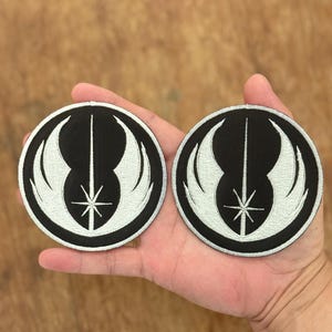 以下が含まれることがあります： スターウォーズの反乱同盟軍のシンボルが描かれた、黒と白の刺繍パッチが2つ。シンボルは、両側に翼があり、中央に星がある白いライトセーバーです。