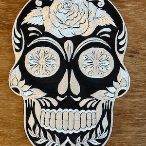 May include: Black and white embroidered sugar skull patch with a white rose and floral details.