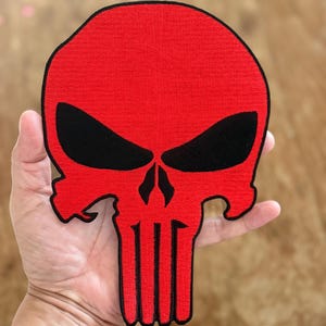 Könnte beinhalten: Roter und schwarzer gestickter Schädel-Patch. Der Schädel hat ein klassisches Punisher-Design mit einem großen, roten Schädel und schwarzen Augenhöhlen.