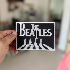Könnte beinhalten: Ein gestickter Patch in Schwarzweiß mit dem legendären "The Beatles"-Logo, auf dem die Bandmitglieder über einen Zebrastreifen laufen.