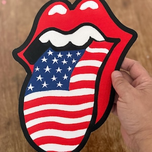 May include: A red and white American flag is printed on a black and white tongue patch. The tongue is sticking out and has a white outline.
