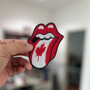 May include: Red, white, and black embroidered patch of a tongue sticking out with a Canadian flag on the tongue.