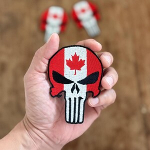 Op de afbeelding: Een geborduurde patch met de Canadese vlag en een schedel met een Punisher-logo, in rood, wit en zwart.